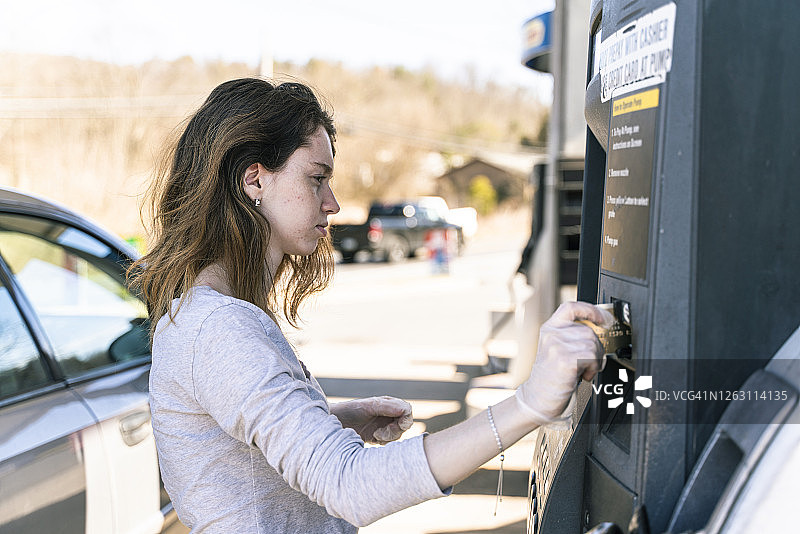 长发女子在加油站为汽车加油，用信用卡在加油机上支付图片素材