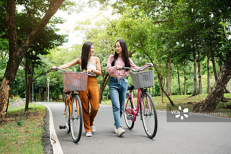 两名亚洲女性在公园里一边骑自行车一边交谈图片素材
