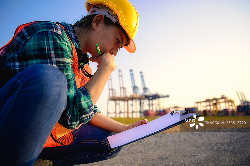 在货运集装箱工作的年轻女码头工人，身穿安全背心，头戴黄色安全帽图片素材