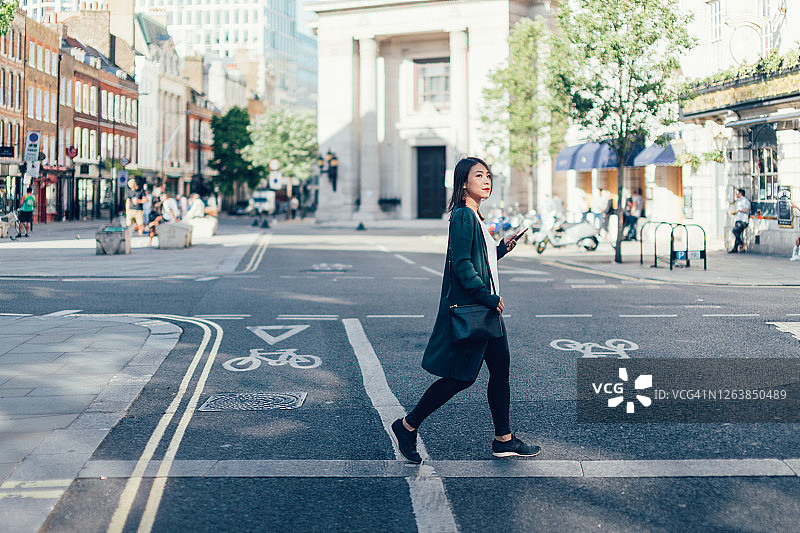 拿着智能手机在城市道路上穿行的年轻女人图片素材