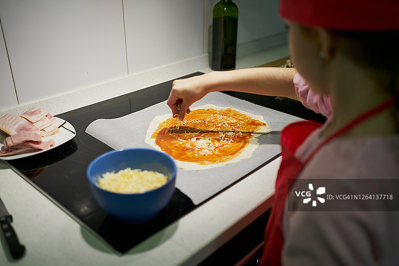 戴红色厨师帽的女孩在披萨面团上加奶酪图片素材