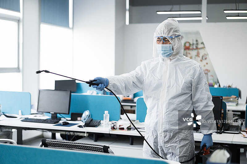 身穿防护服的男人在现代办公室消毒图片素材