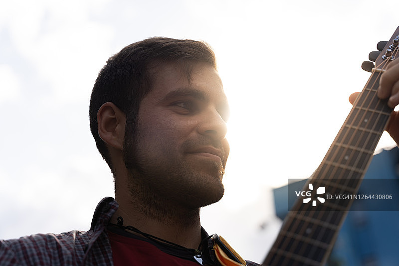 一位吉他手在街头演奏，阳光照在他的脸上，他的笑容合影图片素材