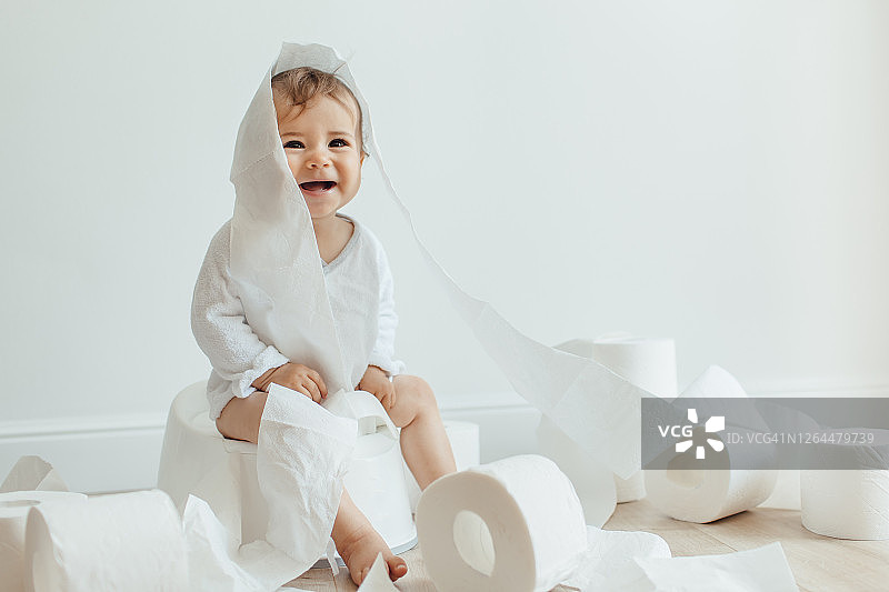 可爱的女宝宝坐在白色便盆上玩卫生纸图片素材