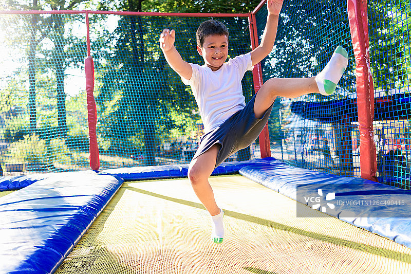 小男孩在蹦床上跳跃，脸上带着灿烂的笑容图片素材
