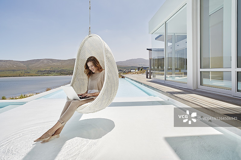 女人坐在游泳池上方的吊椅上使用笔记本电脑图片素材