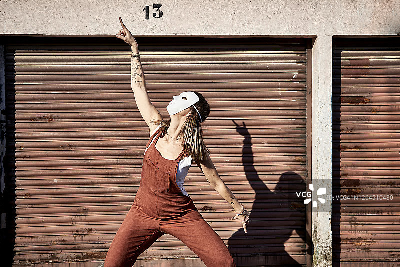 在晴天，戴着白色面具在百叶窗前跳舞的女人图片素材