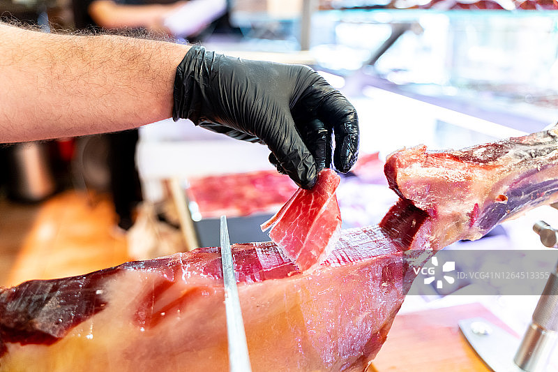 屠夫店里戴着黑色手套的手切割伊比利亚火腿薄片图片素材