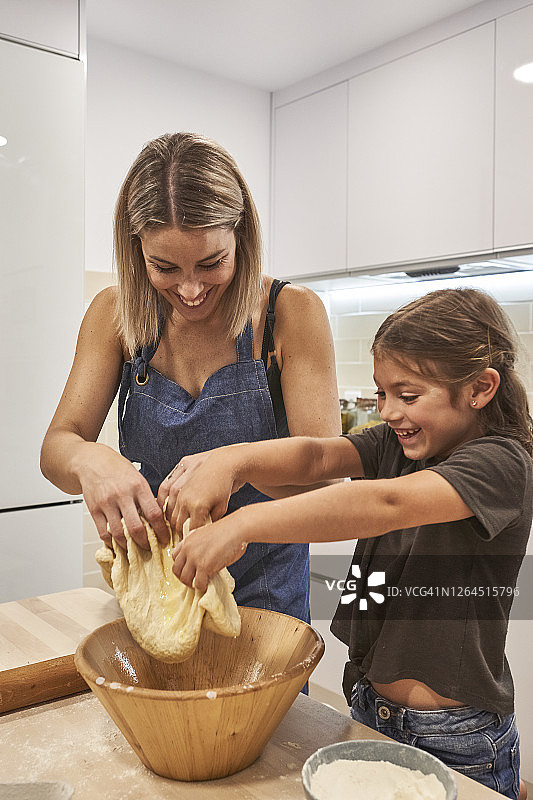 母亲和快乐的女儿在家中揉捏碗里的披萨面团图片素材
