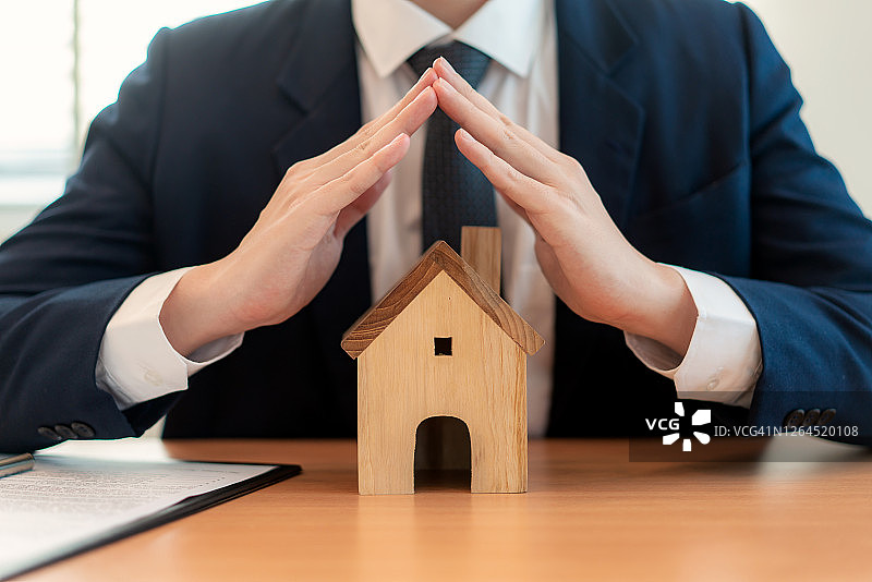 商人双手呵护带屋顶的房子：建筑、安全、房地产概念图片素材