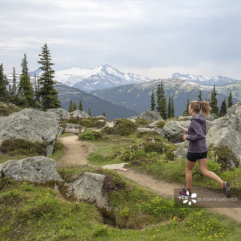 年轻女子在雪山上的高山小径上奔跑图片素材