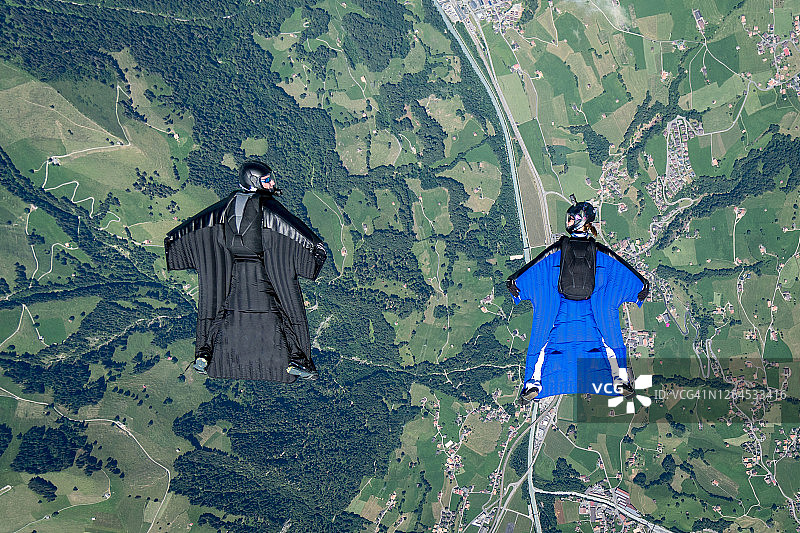 两名翼装飞行员在郁郁葱葱的山谷和道路上空滑翔的航拍视角图片素材