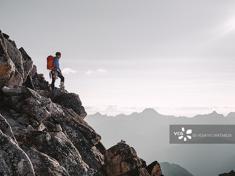 明亮通风的照片：男性登山者在崎岖山坡上仰望太阳图片素材