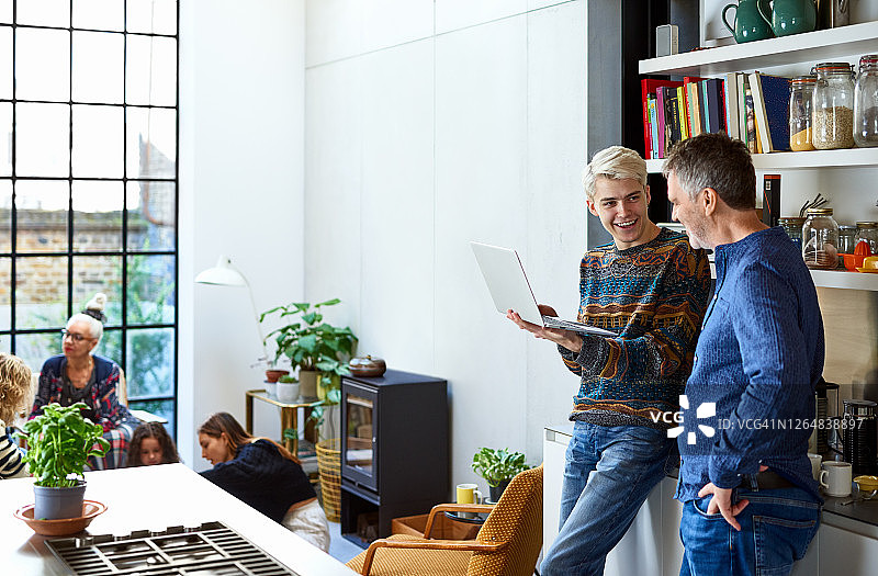 快乐的儿子在厨房里和父亲用笔记本电脑交谈图片素材