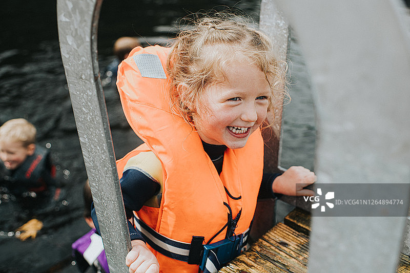 快乐小女孩穿着橙色救生衣爬上码头图片素材