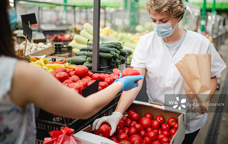 戴防护手套的顾客将番茄递给市场女售货员进行包装图片素材