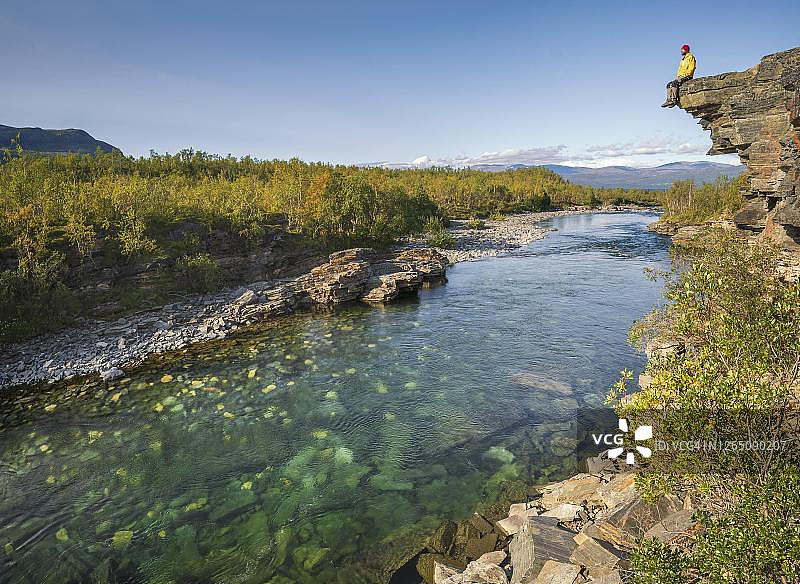 男人坐在阿比斯库国家公园阿比斯库河上的石崖上，位于瑞典图片素材