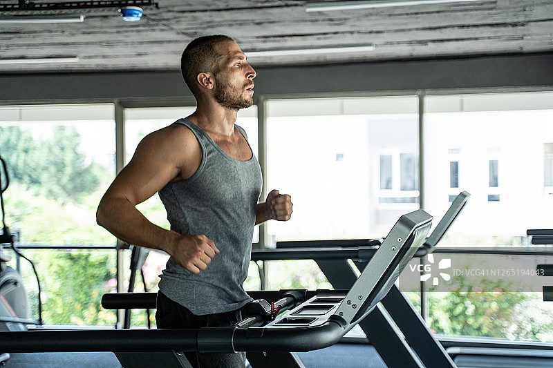年轻英俊的男人在健身房用跑步机做有氧运动图片素材