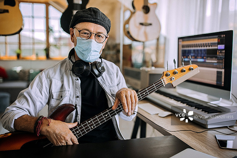 戴着口罩的年长音乐家在他的家庭工作室里摆姿势图片素材
