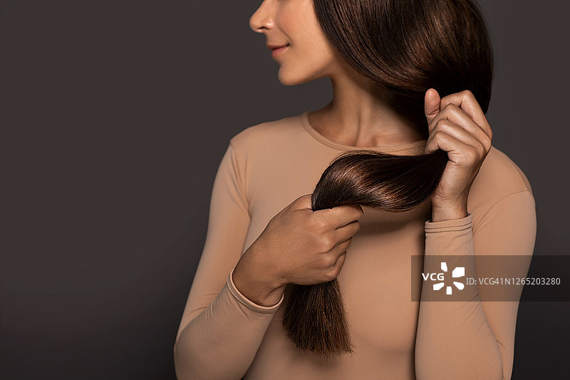 拥有柔顺亮丽长发的棕发女孩，在灰色背景下手持健康秀发，展示美发沙龙理念图片素材