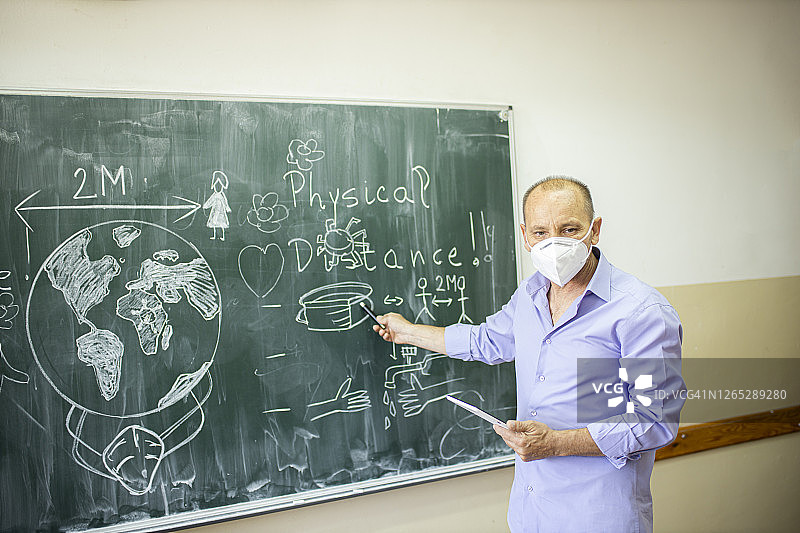在冠状病毒疫情封锁后，戴着防护口罩的老师在学校给学生讲课图片素材