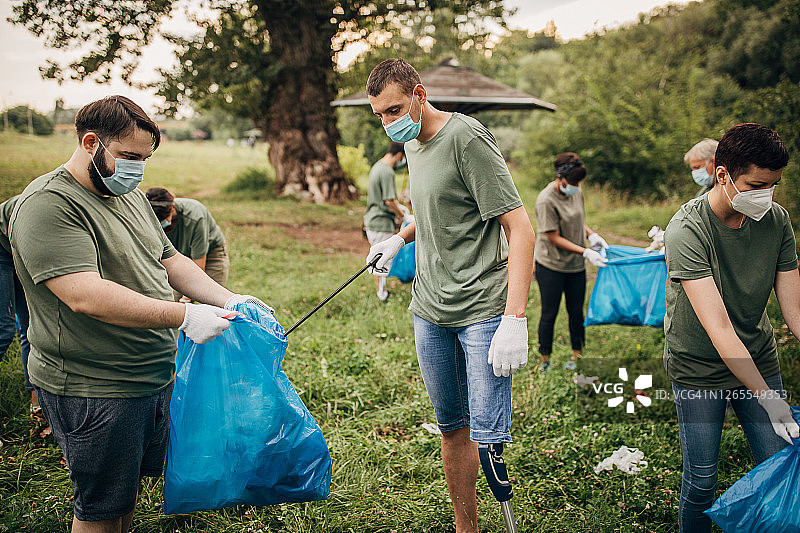 戴着口罩的志愿者和安装假肢的男人一起清理大自然图片素材