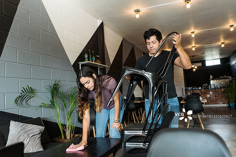 年轻的拉丁情侣在咖啡店清洁并摆放椅子图片素材