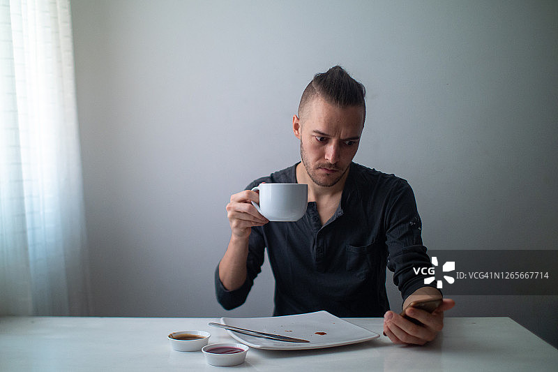 吃完水果吐司后看手机的金发白人男子图片素材