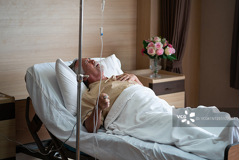躺在病床上、手按紧急呼叫按钮的亚洲老人患者图片素材