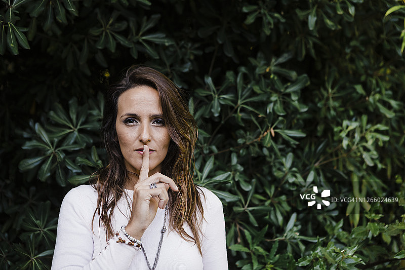 公园里，手指放在嘴唇上的美丽女子图片素材