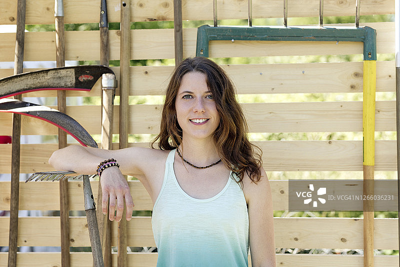 拿着园艺设备站在栅栏前的卷发年轻女人图片素材