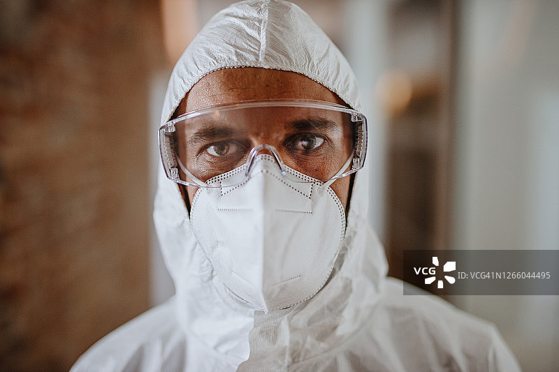 身穿防护服和口罩的男人在办公室喷洒消毒剂的特写图片素材