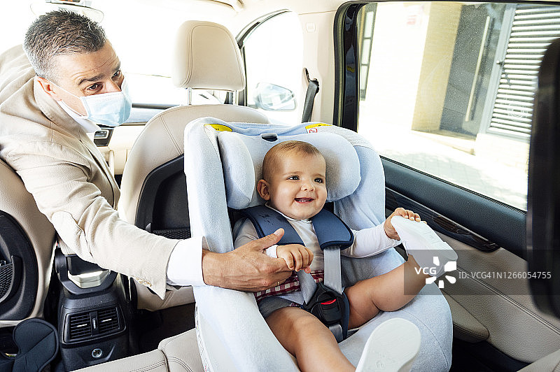 父亲戴着防护口罩，男婴坐在车里的儿童座椅上图片素材
