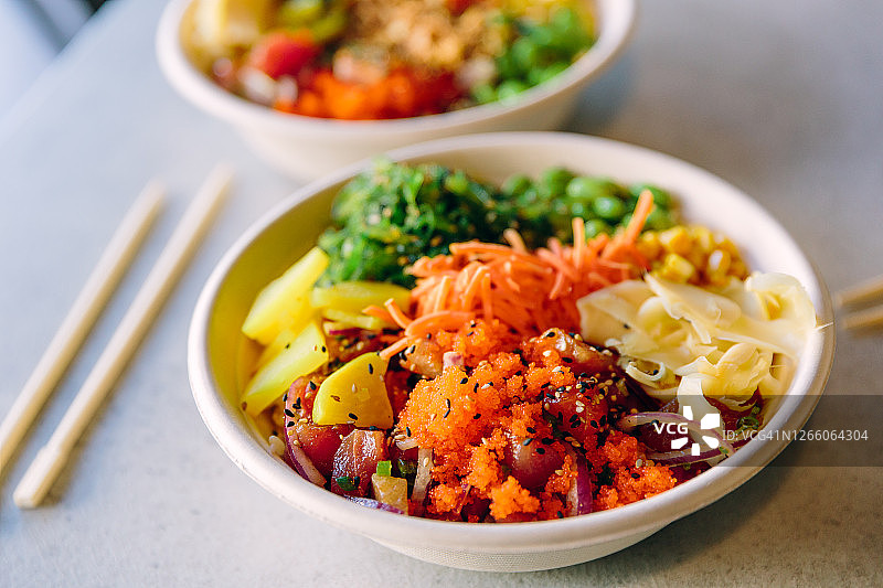 含三文鱼、金枪鱼和各种蔬菜的盖饭特写，用可回收纸盘盛装图片素材