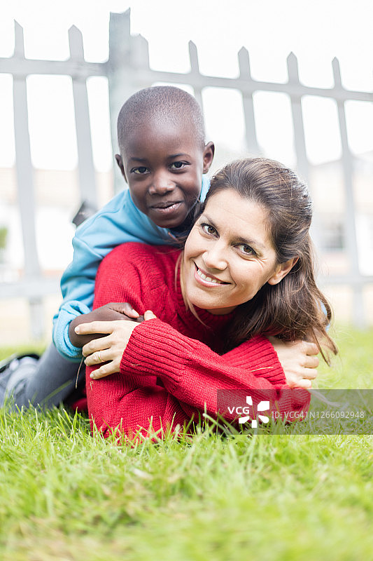 年轻漂亮的母亲和她的养子在公园草地上躺着，都对着镜头微笑图片素材