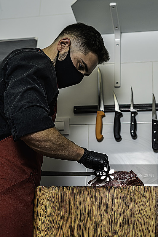 戴着口罩在木头上切割生肉的屠夫图片素材