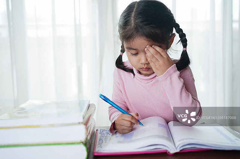 表情严肃的亚洲学龄前女童在写作业，思考如何完成家庭作业。聪慧，教育和聪明的学习理念。图片素材
