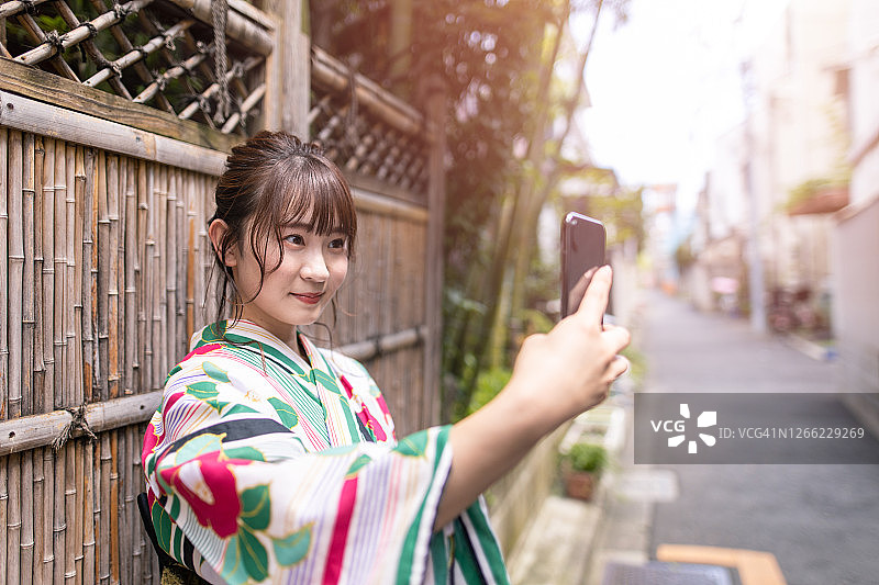 身穿浴衣的年轻女人靠在竹墙上自拍图片素材