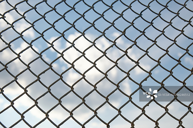 蓝色天空与白色云朵下的金属丝网围栏，限制自由的概念图片素材