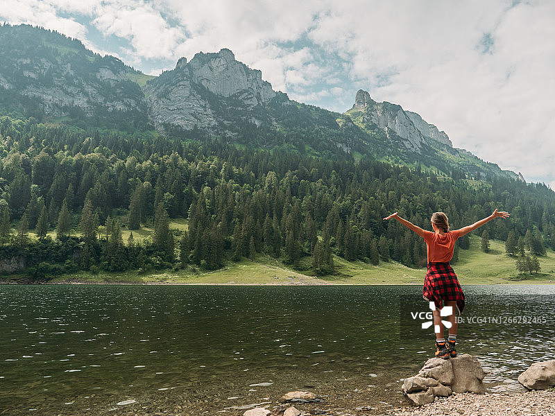 女人站在美丽的阿尔卑斯湖边，张开双臂图片素材