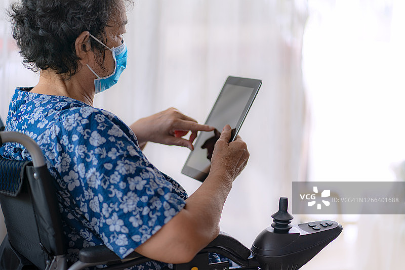 老年妇女戴着口罩在电动轮椅上使用平板电脑图片素材