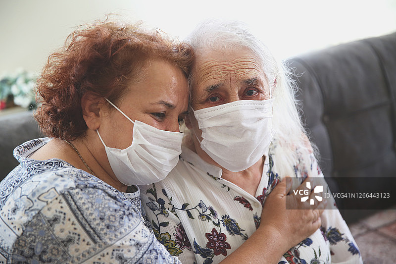 情绪低落的老年母亲和女儿戴着医用口罩哭泣拥抱，悲痛地失去亲人，与冠状病毒作斗争，受新冠肺炎疫情影响的人们和家庭图片素材