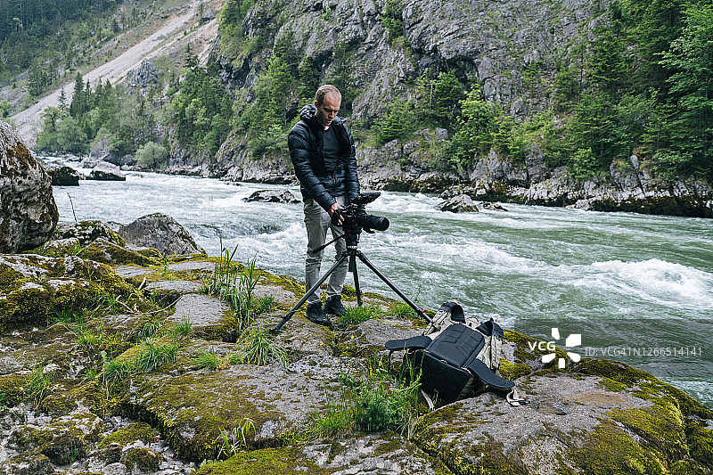 男人用安装在三脚架上的胶片相机拍摄流动的河流图片素材