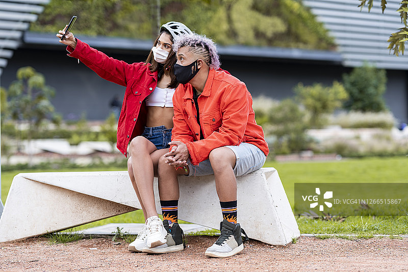 疫情期间戴着口罩的拉丁裔情侣在街上自拍，他们穿着运动服，看起来非常高兴图片素材