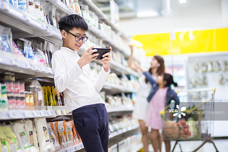 在食品店里，中国青少年玩手机，母亲在挑选食物图片素材
