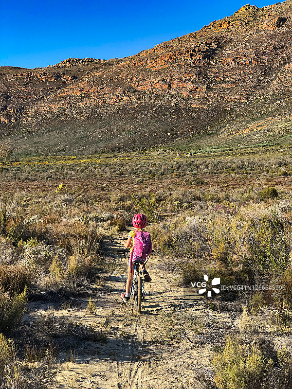 背着背包在荒野小路上越野骑行的年轻女孩图片素材