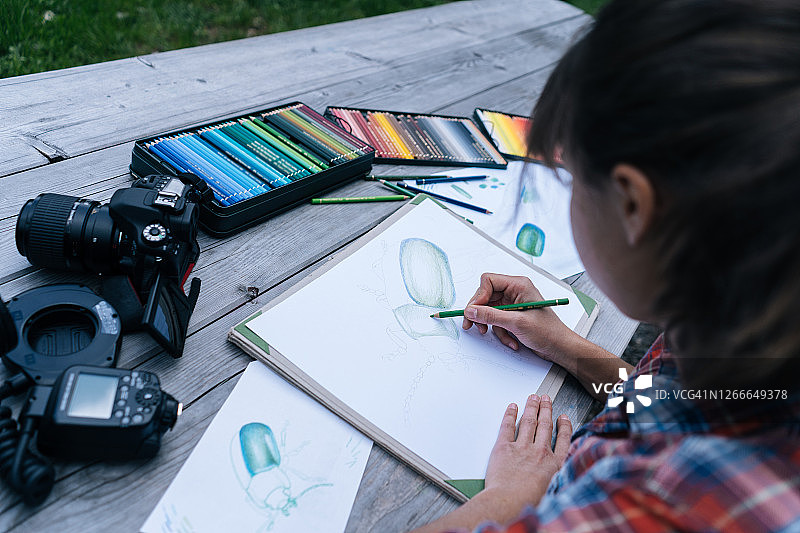 年轻女艺术家在小屋外的木桌上用彩色铅笔绘画图片素材