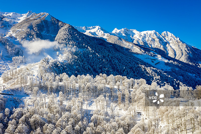 俄罗斯索契罗莎库塔滑雪胜地的冬季山景，雾凇树木映衬着美丽的晨曦，雪炮在山坡上喷洒雪花图片素材