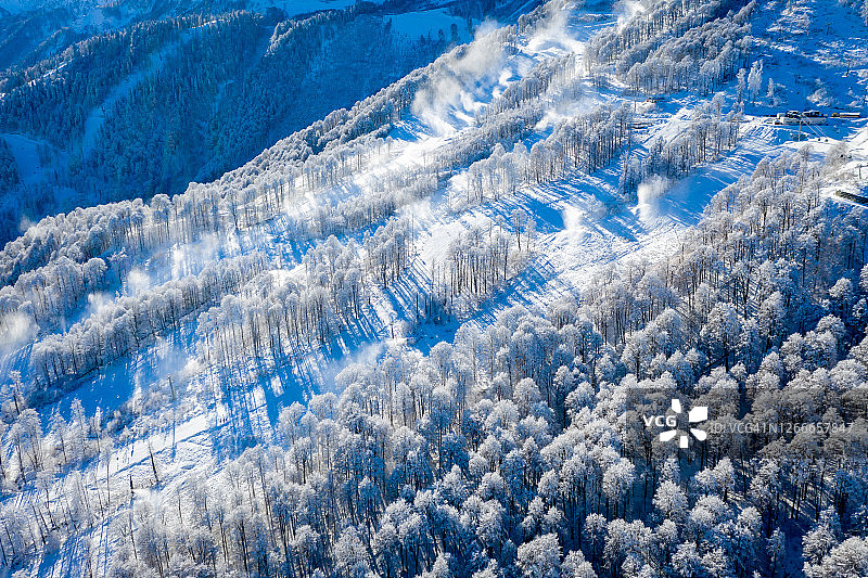 俄罗斯索契罗莎库塔滑雪胜地的冬季山景，雾凇树木映衬着美丽的晨曦，雪炮在山坡上喷洒雪花图片素材