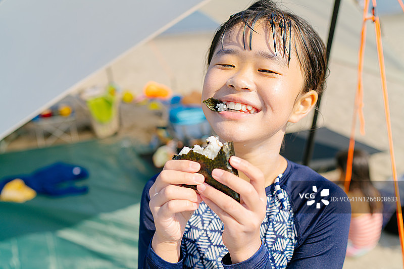 在海滩高兴地吃饭团的小女孩图片素材